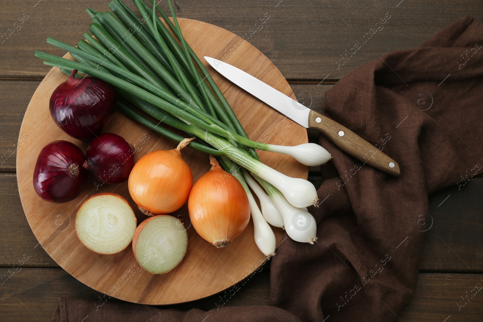 Photo of Board with different kinds of onions on wooden table, top view