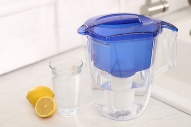 Photo of Water filter jug, glass and lemons on countertop in kitchen