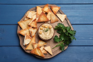 Photo of Delicious pita chips with hummus on blue wooden table, top view