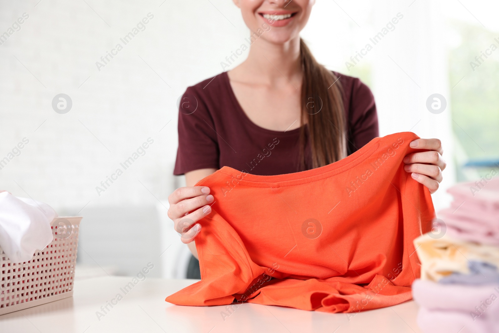 Photo of Happy young woman with clean t-shirt at table, closeup. Laundry day