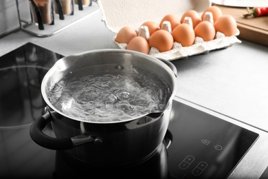 Pot with boiling water on electric stove in kitchen, space for text