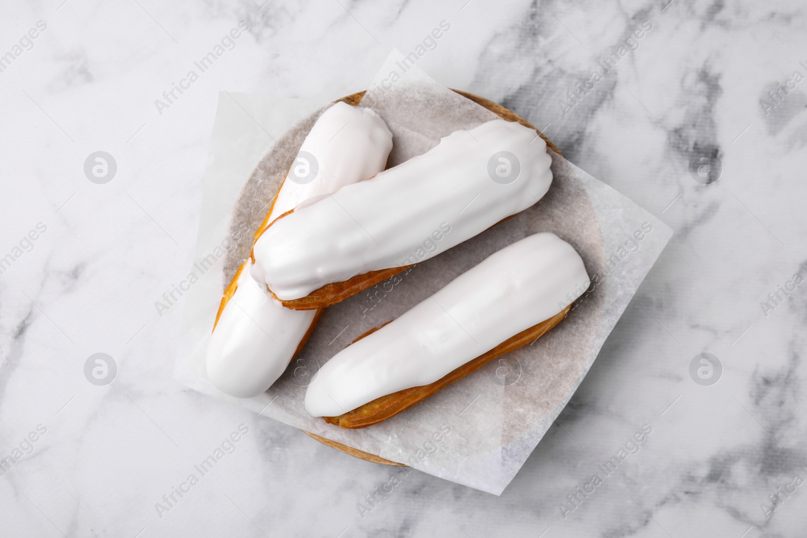 Photo of Delicious eclairs covered with glaze on white marble table, top view
