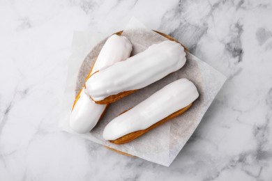 Photo of Delicious eclairs covered with glaze on white marble table, top view