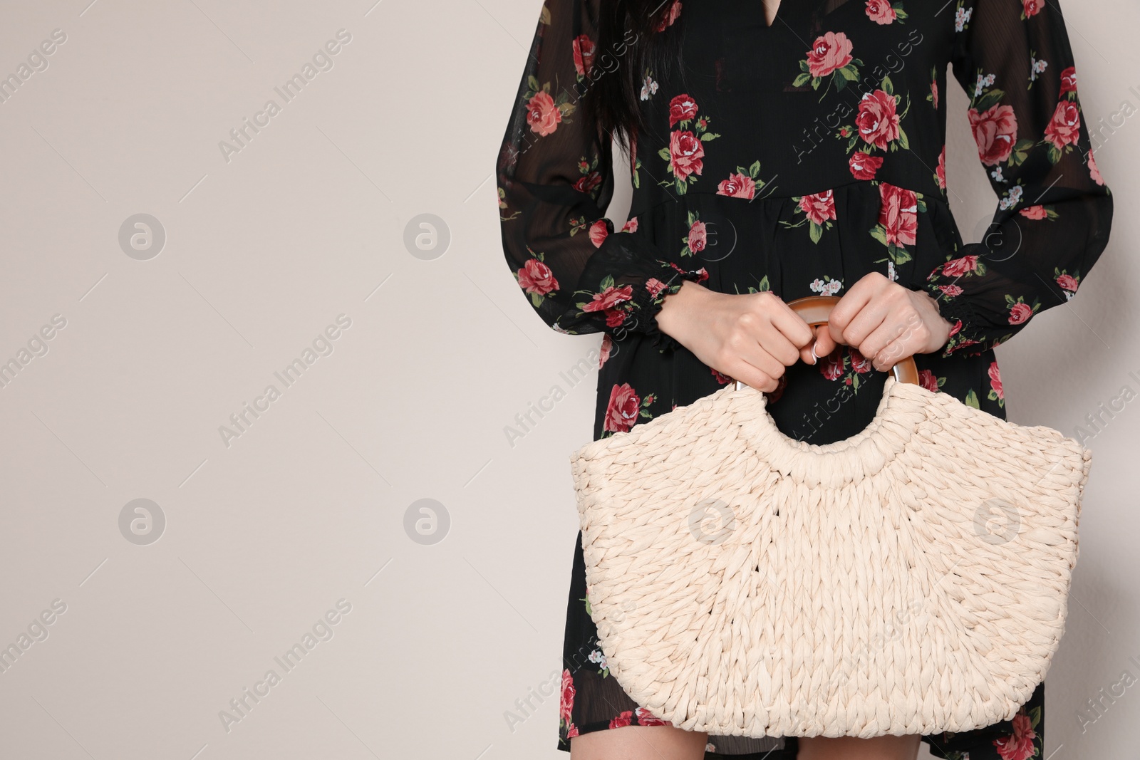 Photo of Young woman wearing floral print dress with straw bag on beige background, closeup. Space for text