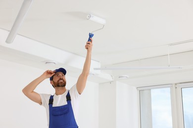 Photo of Handyman painting ceiling with roller in room