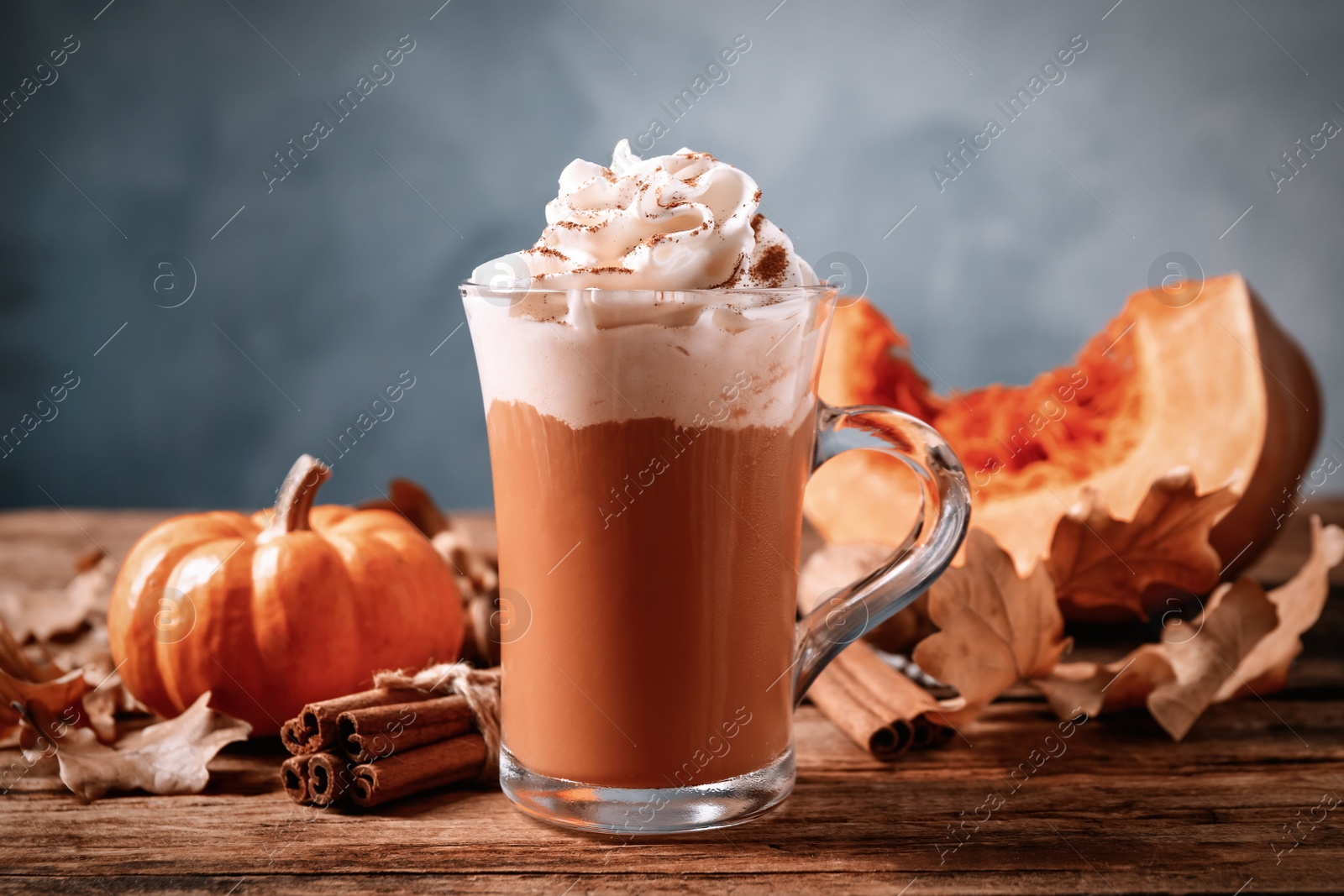 Photo of Delicious pumpkin latte and cinnamon on wooden table, closeup