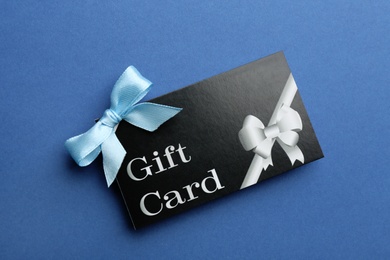 Photo of Gift card with bow on blue background, top view
