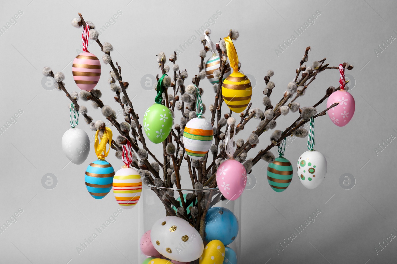 Photo of Vase with beautiful willow branches and painted Easter eggs on light grey background