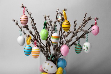 Photo of Vase with beautiful willow branches and painted Easter eggs on light grey background