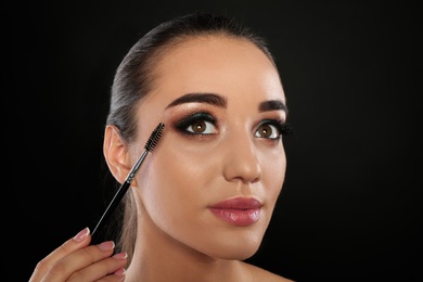 Photo of Portrait of young woman with eyelash extensions holding brush on black background