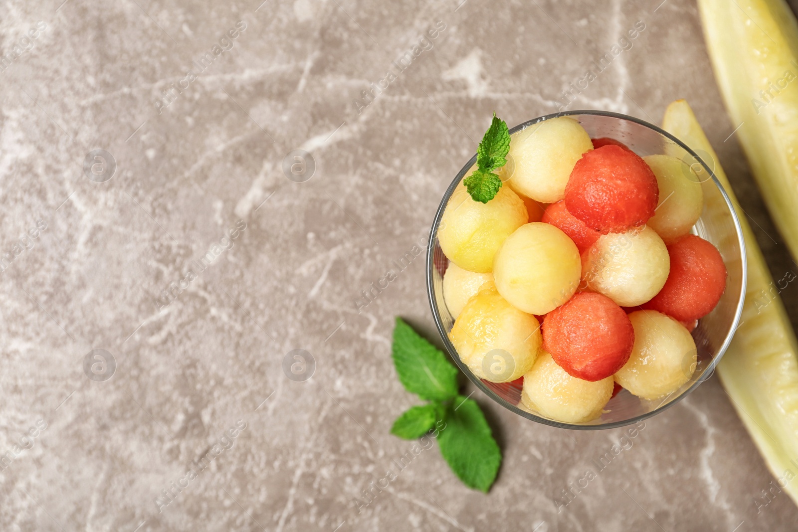 Photo of Bowl of melon and watermelon balls on brown marble table, top view. Space for text