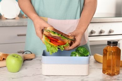 Photo of Woman packing food for her child at table in kitchen, closeup. Healthy school lunch