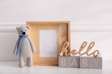 Photo of Empty photo frame, cute toy bear and decor near wall, space for text. Baby room interior element