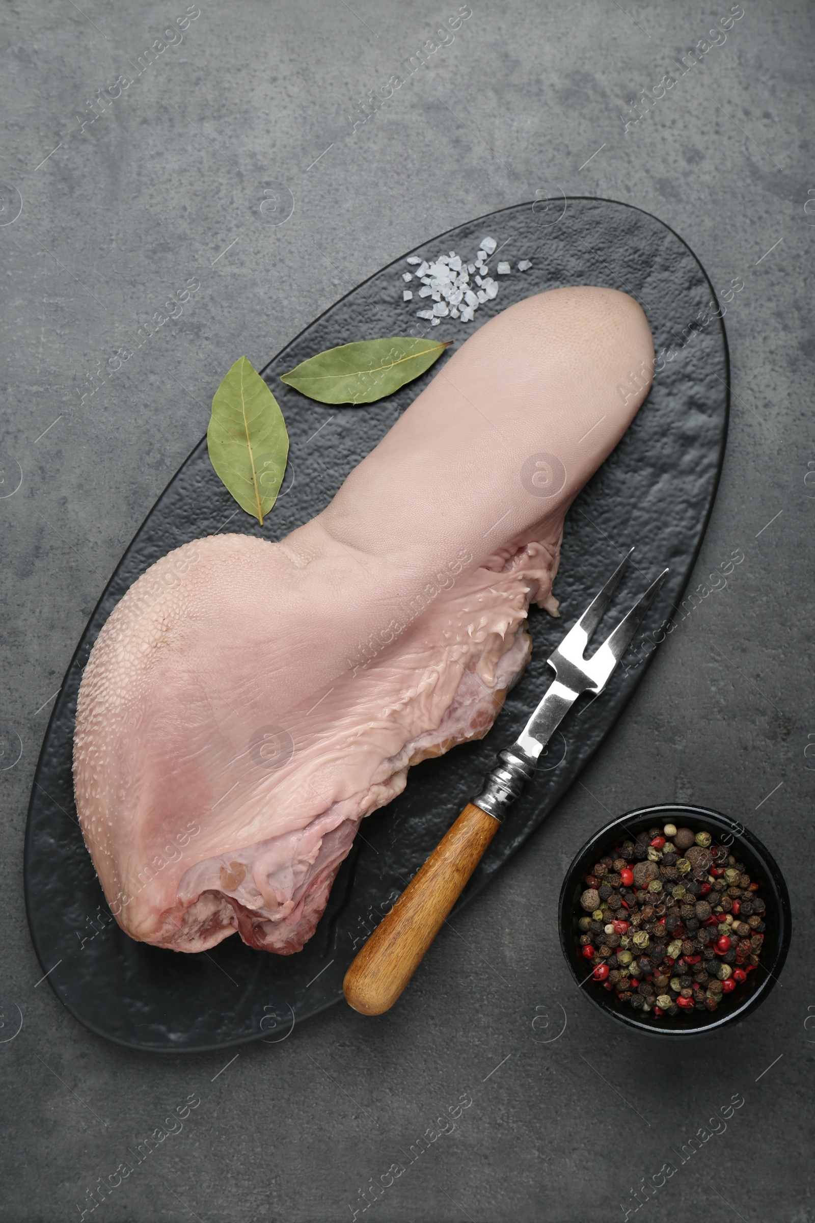 Photo of Serving board with raw beef tongue, peppercorns and bay leaves on grey table, flat lay