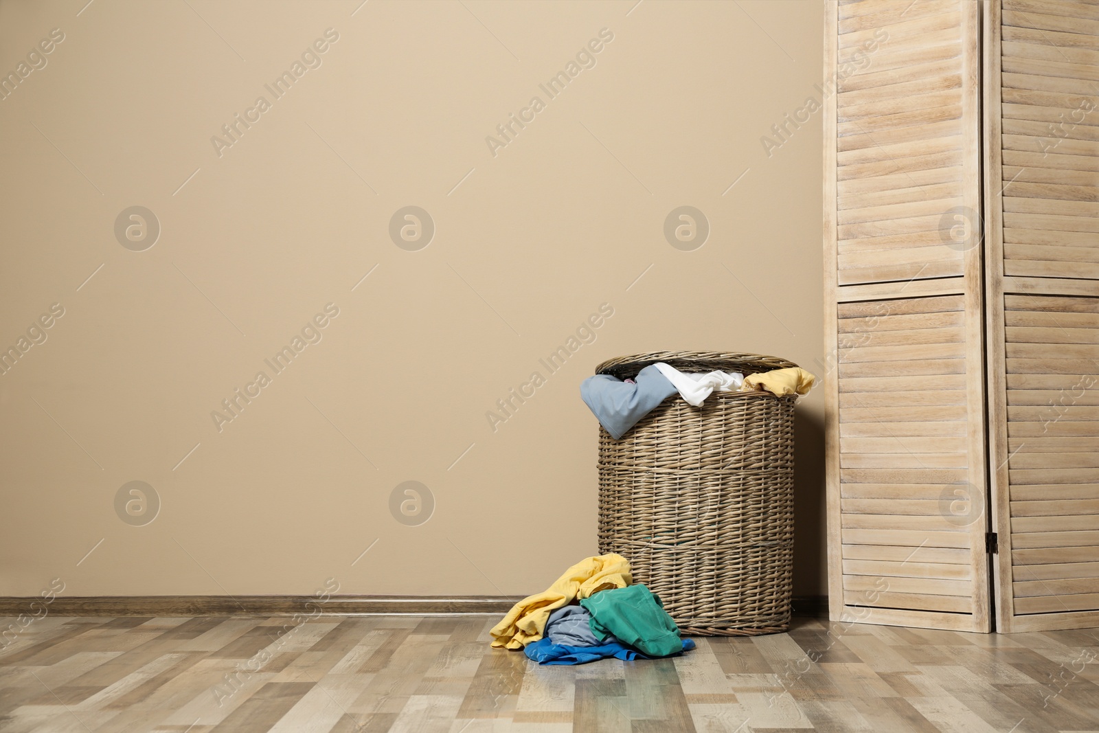 Photo of Wicker laundry basket full of dirty clothes on floor near wall. Space for text