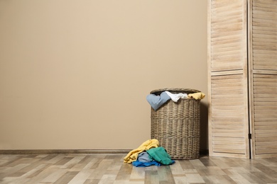 Wicker laundry basket full of dirty clothes on floor near wall. Space for text