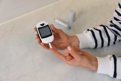 Photo of Diabetes. Woman checking blood sugar level with glucometer at light table, closeup