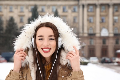Photo of Beautiful young woman listening to music with headphones outdoors. Space for text