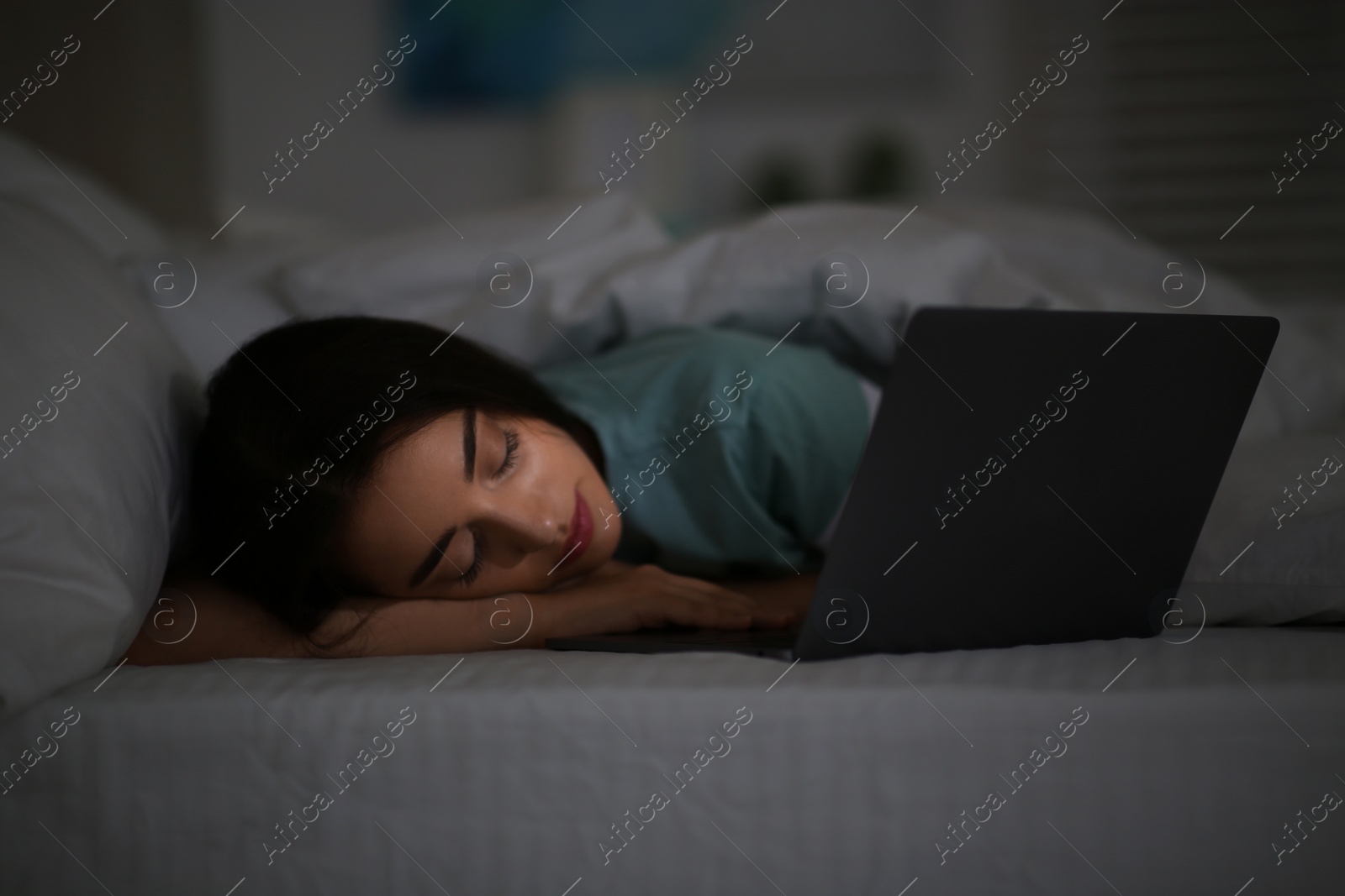 Photo of Young woman with nomophobia sleeping near laptop in bed at night