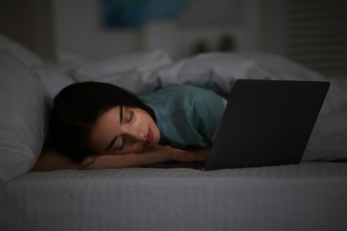Photo of Young woman with nomophobia sleeping near laptop in bed at night