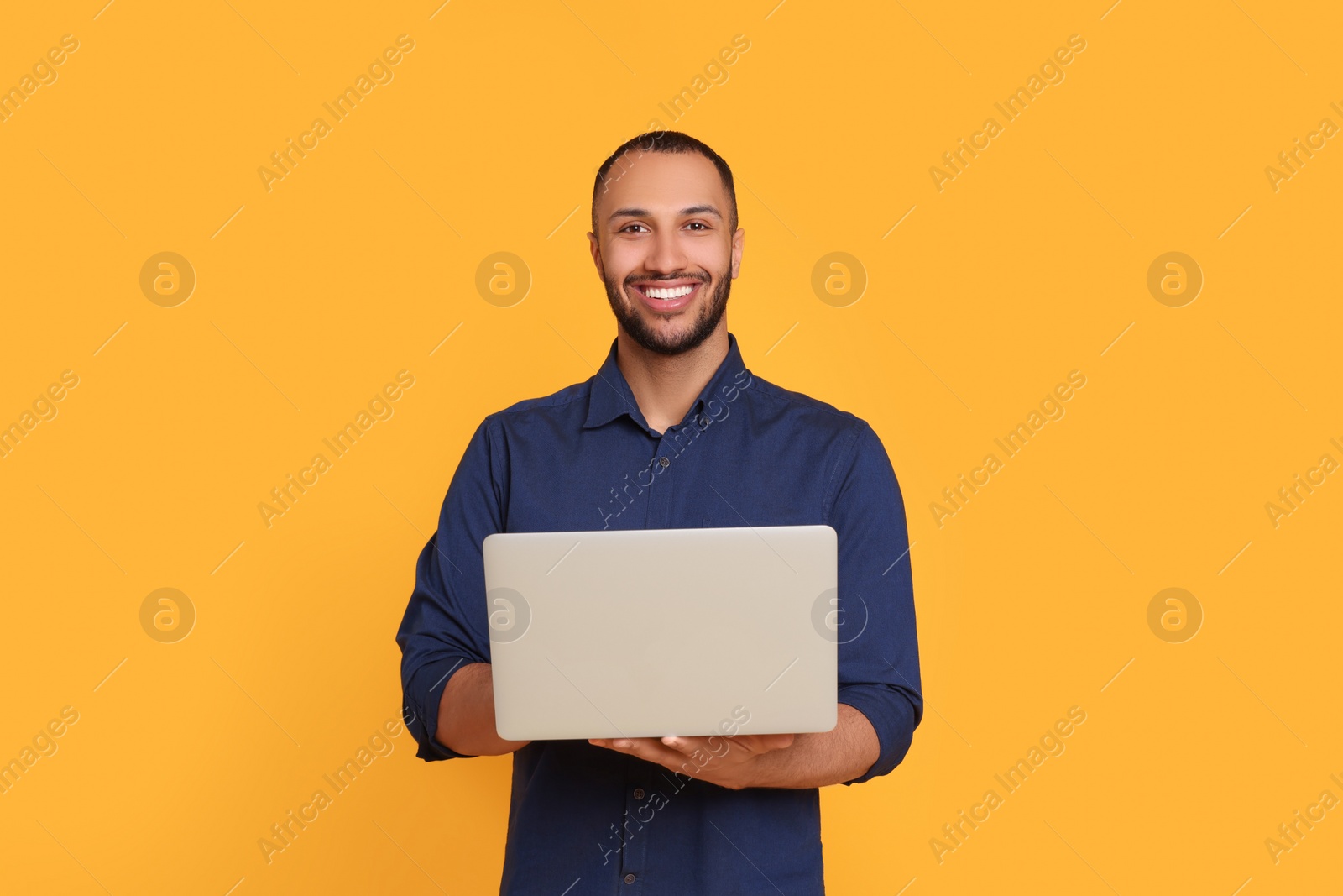 Photo of Smiling young man working with laptop on yellow background