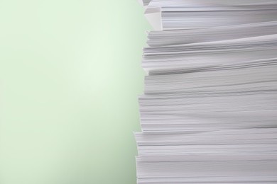 Photo of Stack of paper sheets on light green background, closeup. Space for text