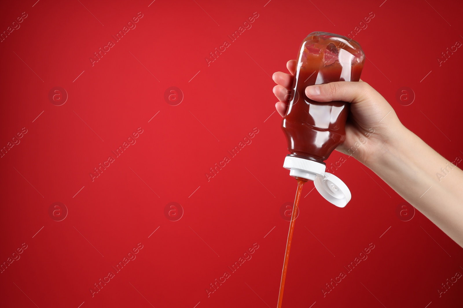 Photo of Woman pouring tasty ketchup from bottle on red background, closeup. Space for text