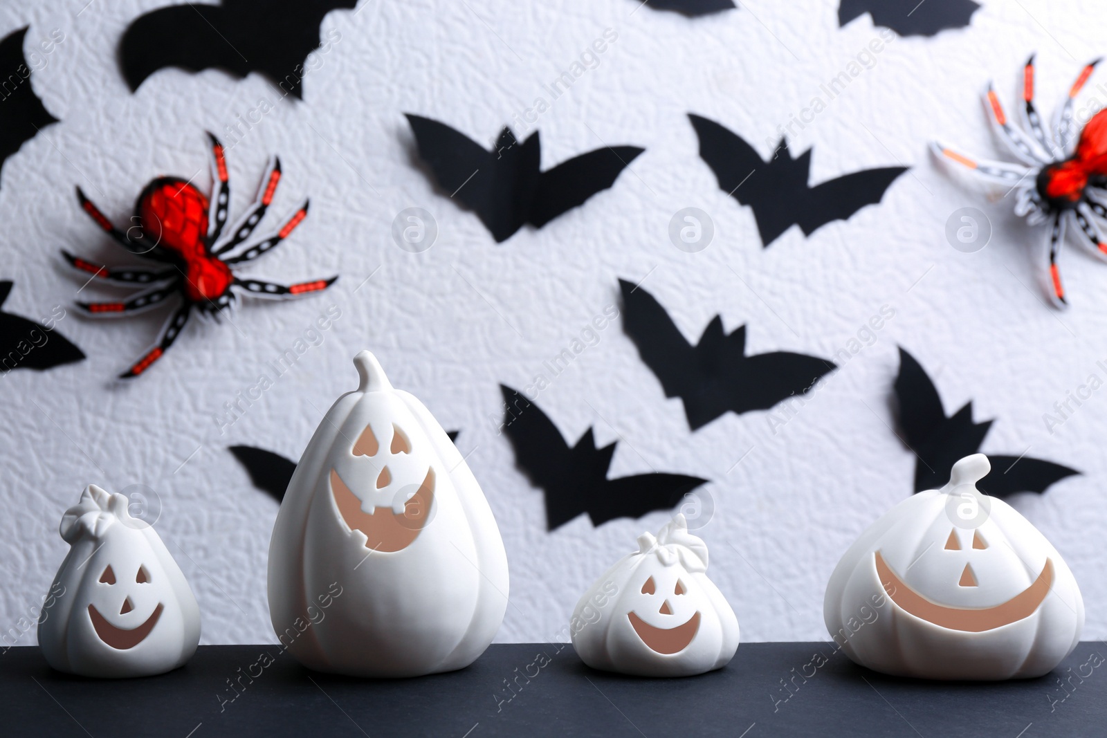 Photo of Composition with pumpkin shaped candle holders on black table against white background. Halloween decoration