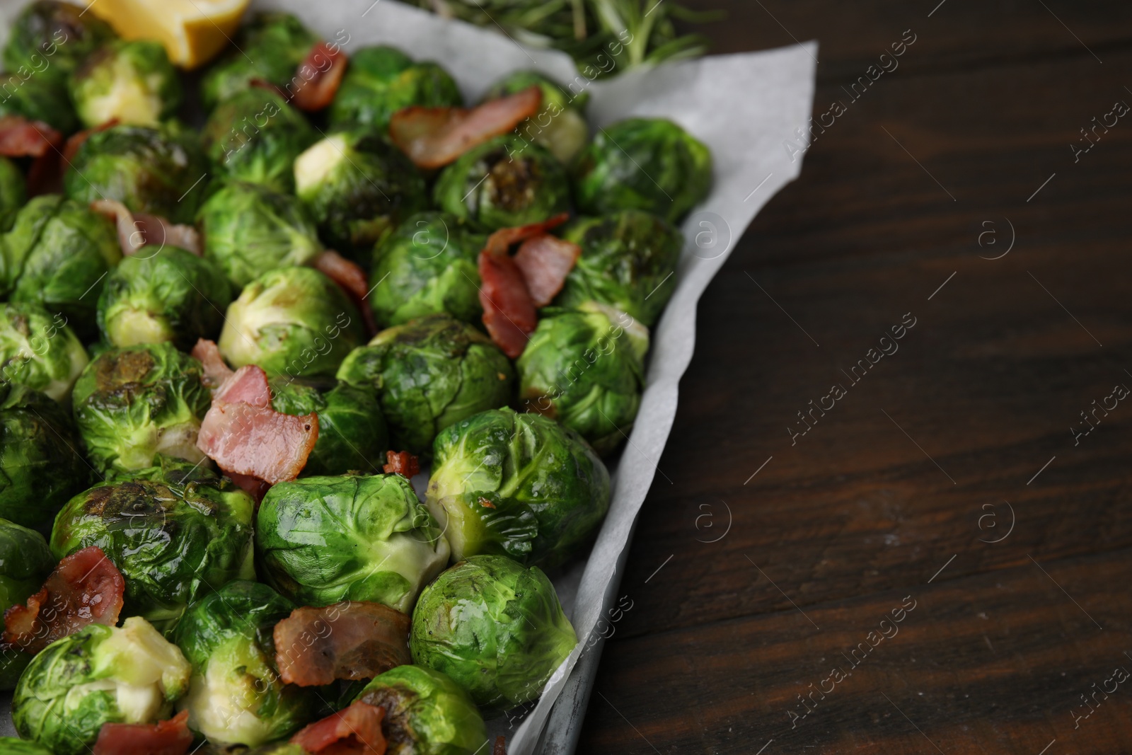 Photo of Delicious roasted Brussels sprouts and bacon in baking dish on wooden table, closeup. Space for text