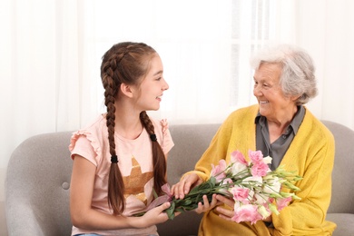 Photo of Cute girl congratulating her grandmother in living room