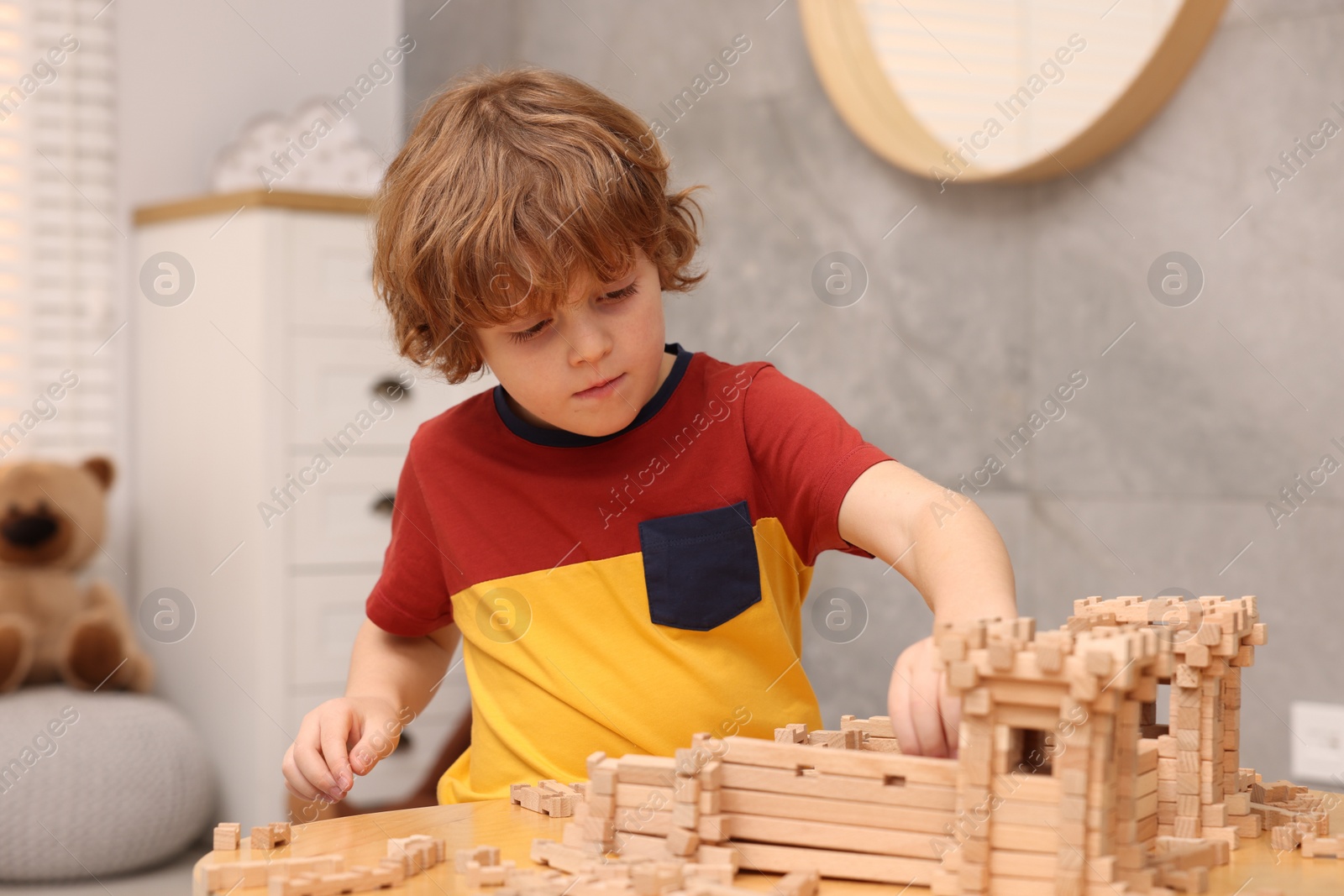 Photo of Little boy playing with wooden entry gate at table in room. Child's toy