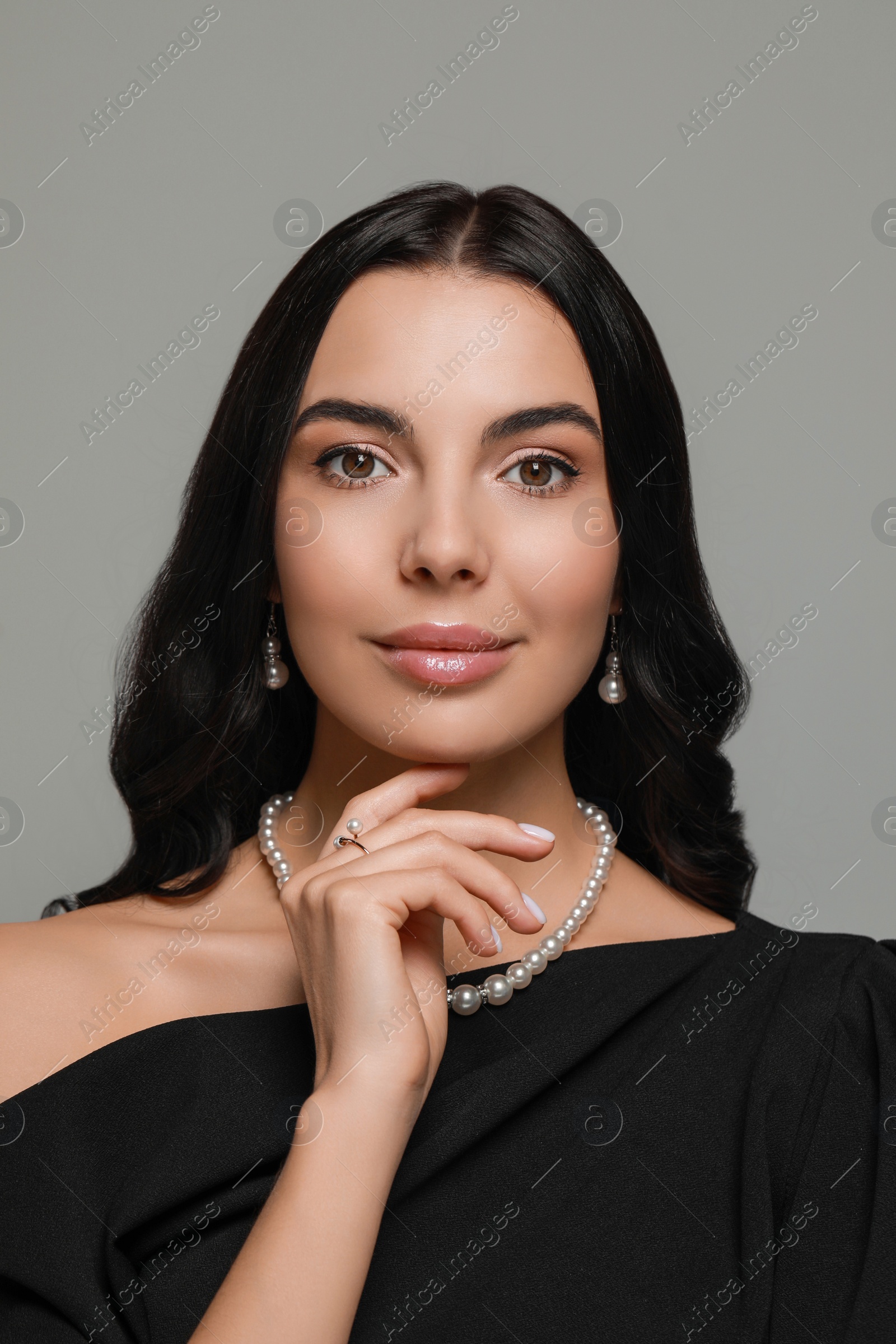 Photo of Young woman wearing elegant pearl jewelry on grey background