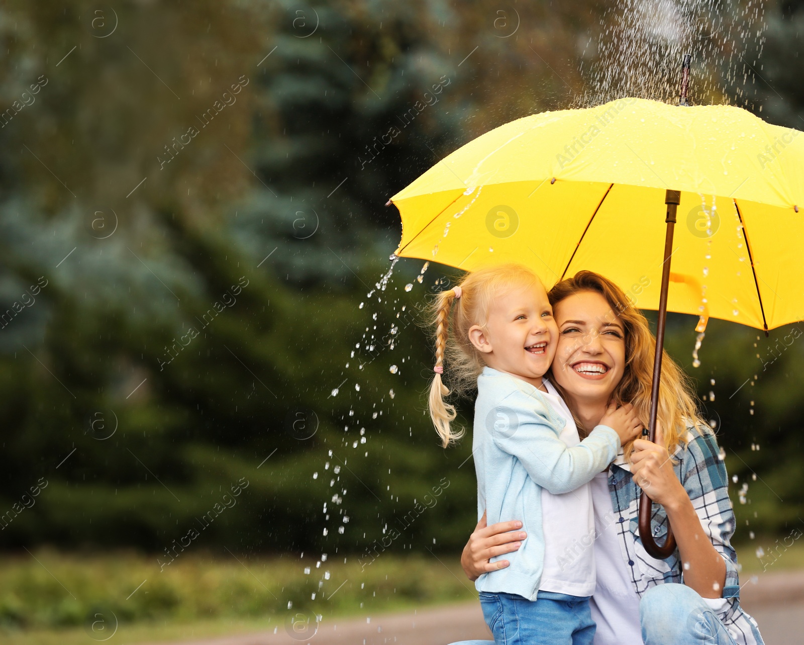 Photo of Happy mother and daughter with umbrella under rain in park. Space for text