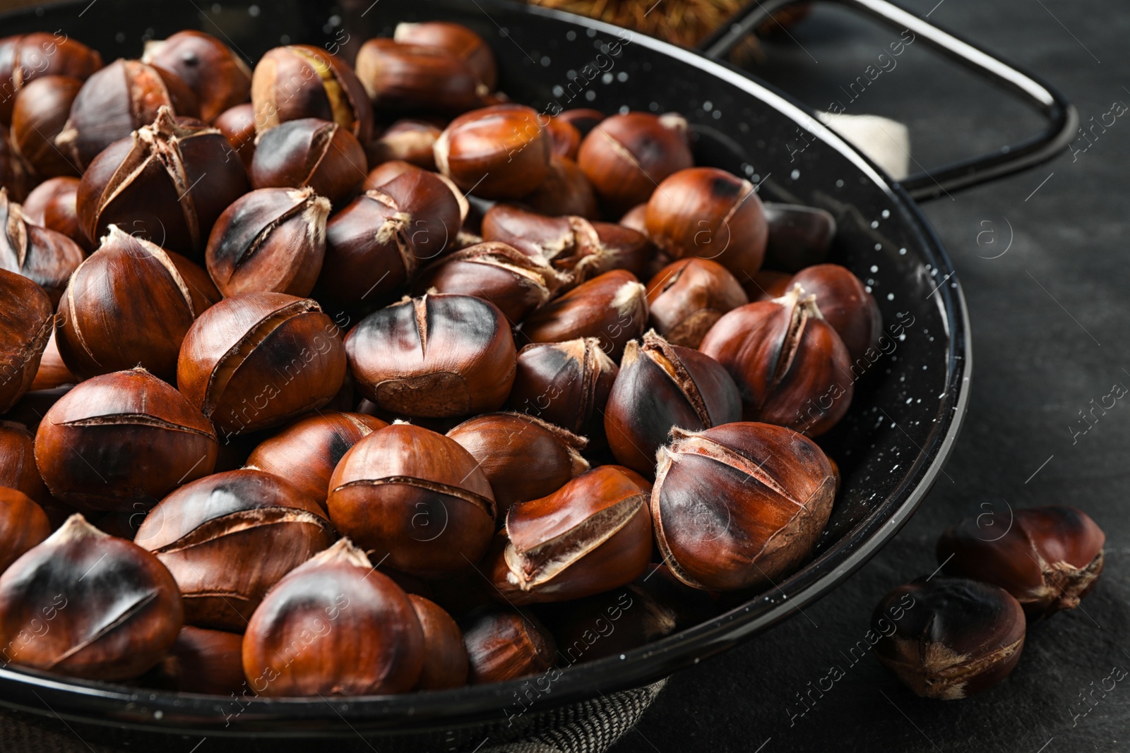 Photo of Delicious roasted edible chestnuts in frying pan on black table, closeup