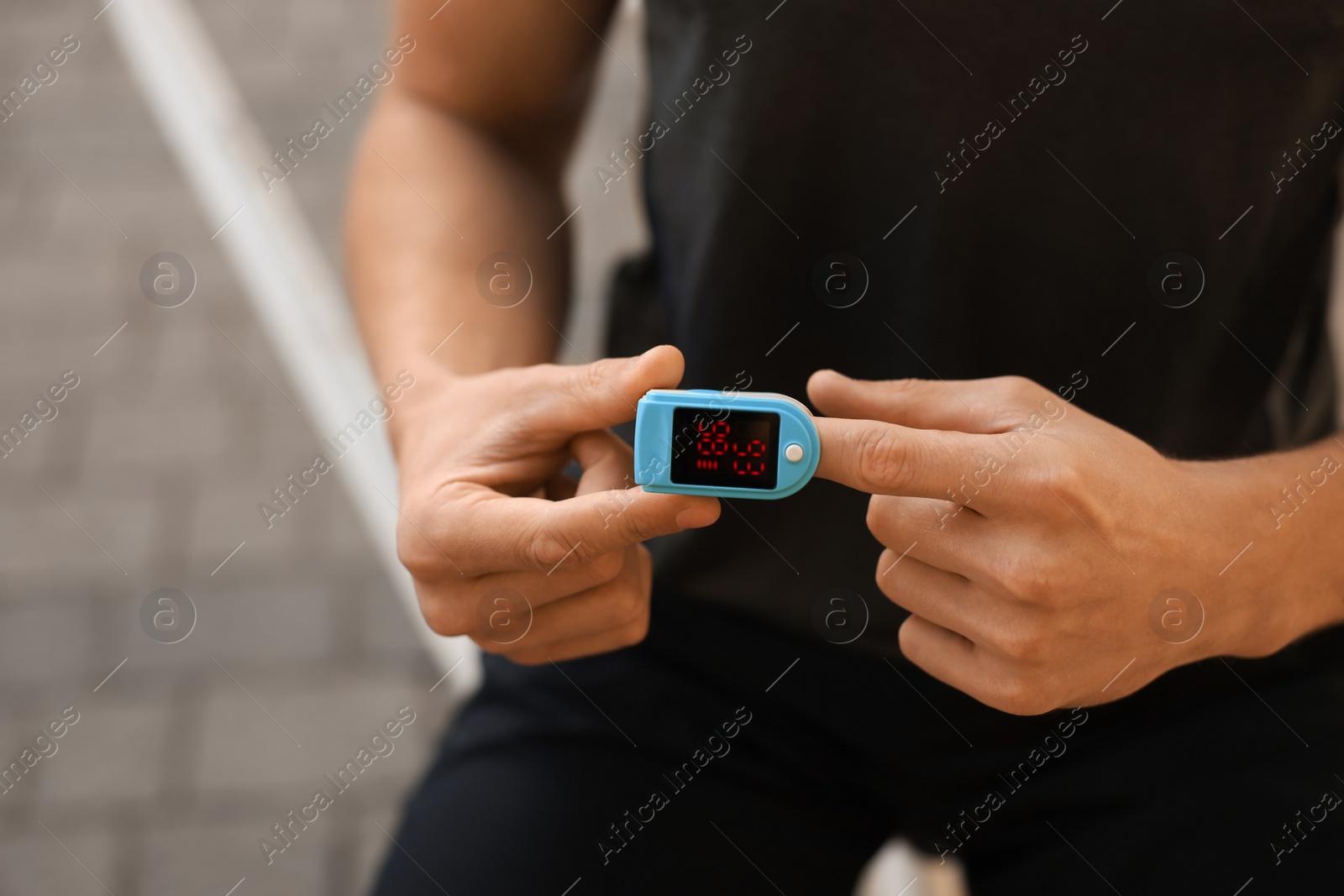 Photo of Man checking pulse with blood pressure monitor on finger after training outdoors, closeup. Space for text