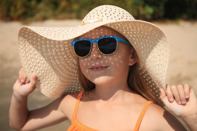 Photo of Little girl in stylish sunglasses and hat on beach