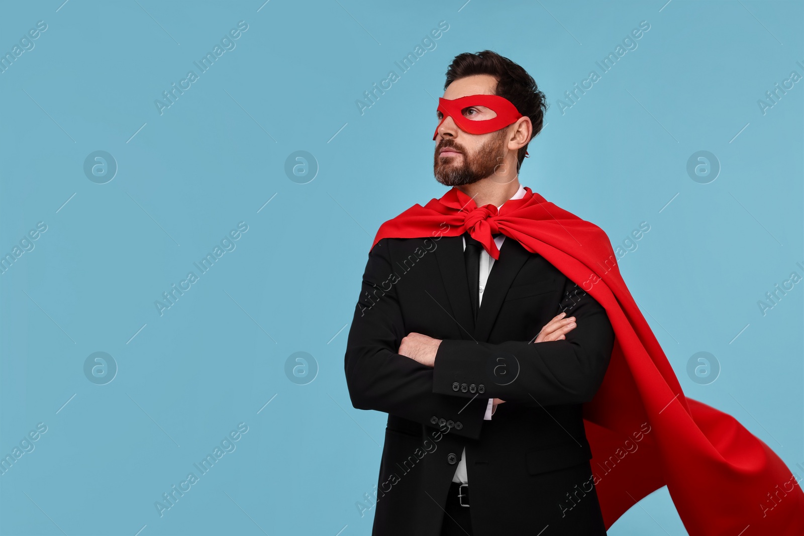 Photo of Businessman wearing red superhero cape and mask on light blue background. Space for text