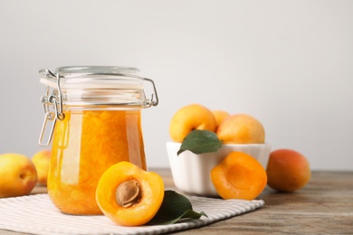 Photo of Jar of apricot jam and fresh fruits on wooden table