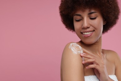 Photo of Beautiful young woman applying body cream onto shoulder on pink background, space for text
