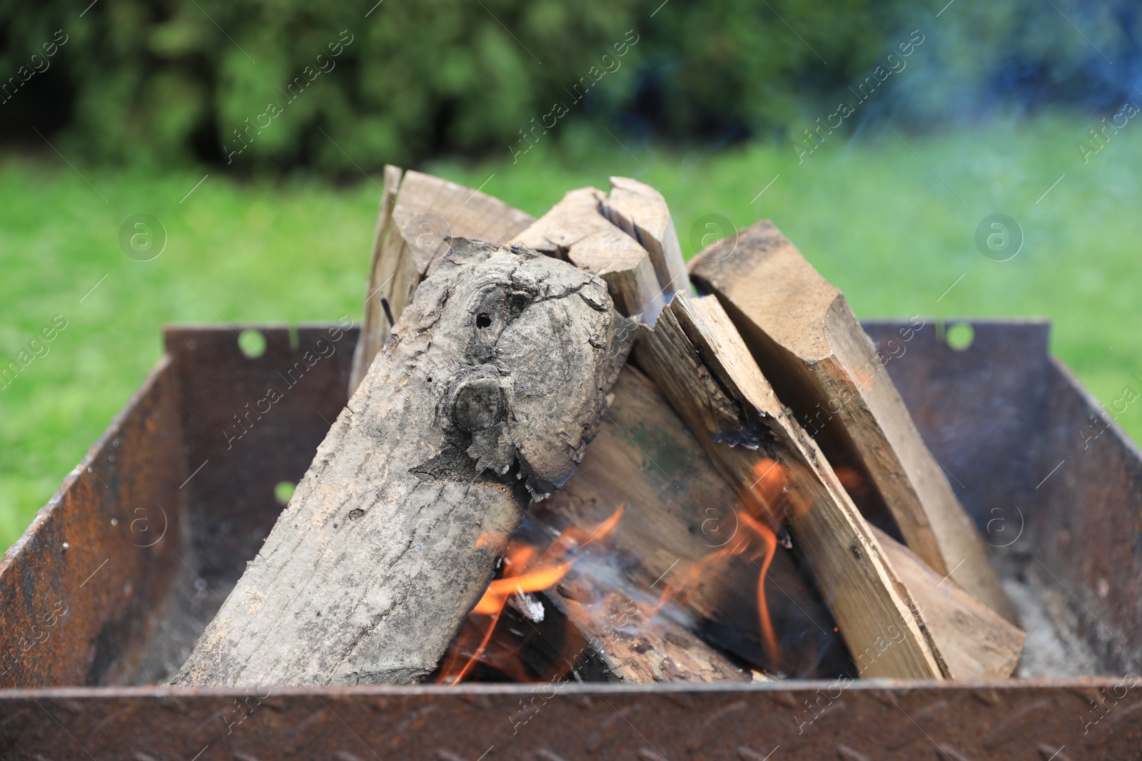 Photo of Metal brazier with burning firewood outdoors, closeup