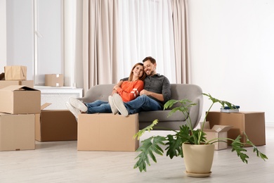 Photo of Couple resting on sofa near moving boxes in their new house