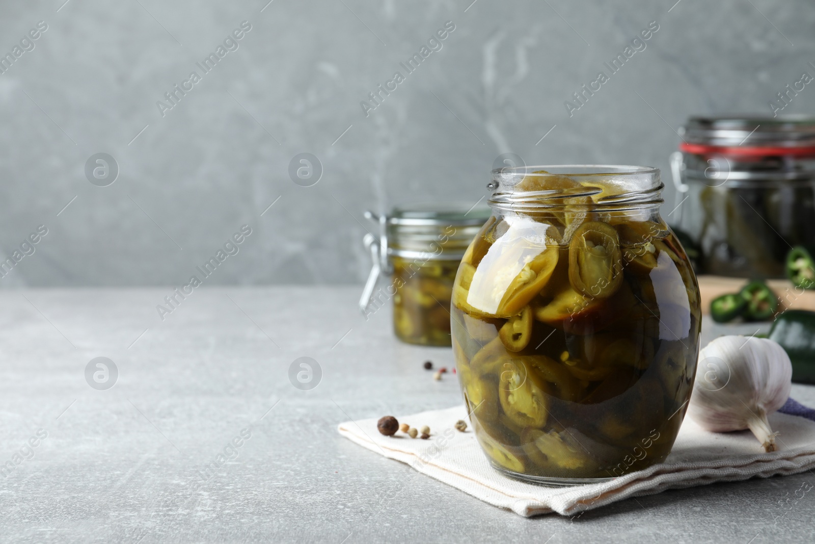 Photo of Glass jar with slices of pickled green jalapeno peppers on light grey table, space for text