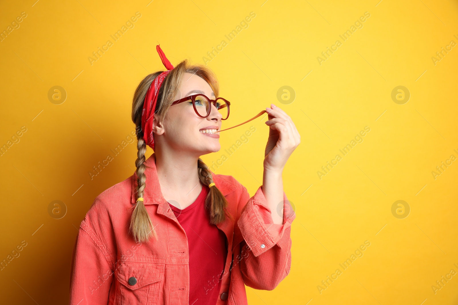 Photo of Fashionable young woman with braids and bright makeup chewing bubblegum on yellow background, space for text