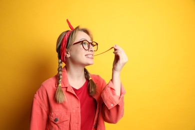 Fashionable young woman with braids and bright makeup chewing bubblegum on yellow background, space for text