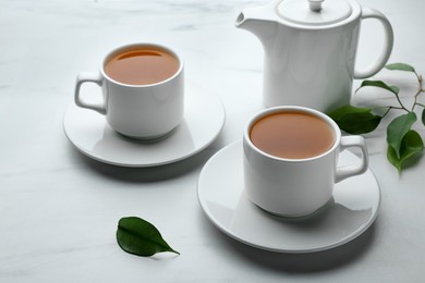 Green tea in cups with leaves and teapot on white marble table