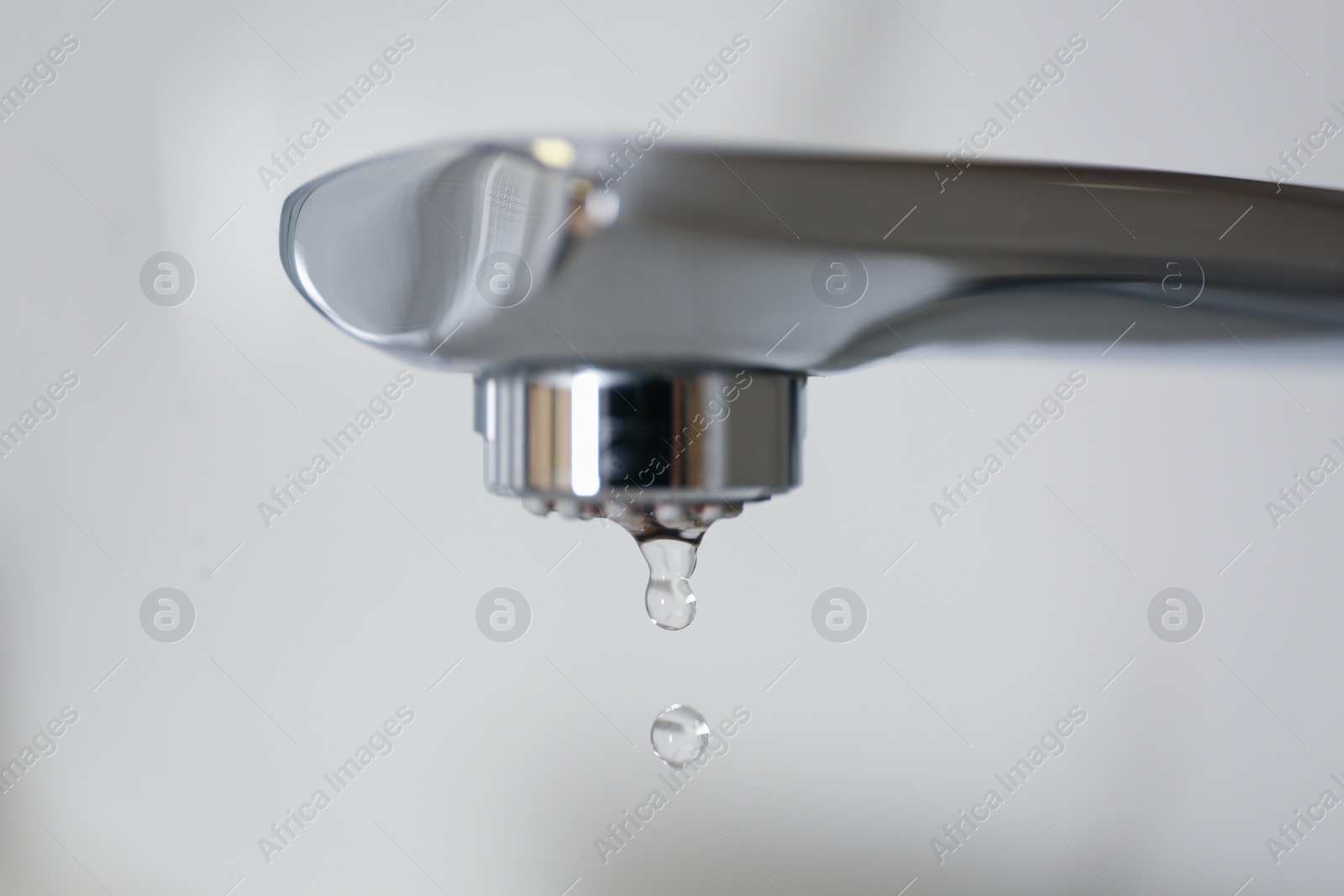 Photo of Water drops falling down from tap on light background, closeup