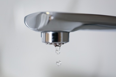 Water drops falling down from tap on light background, closeup