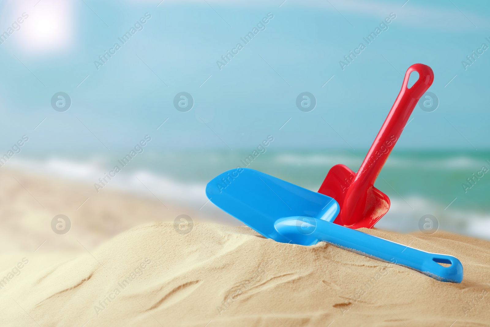 Image of Red and blue plastic toy shovels on sandy beach near sea, space for text 