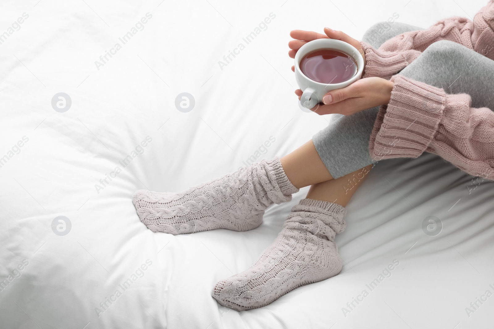 Photo of Woman with cup of tea wearing warm socks in comfortable bed, closeup. Space for text