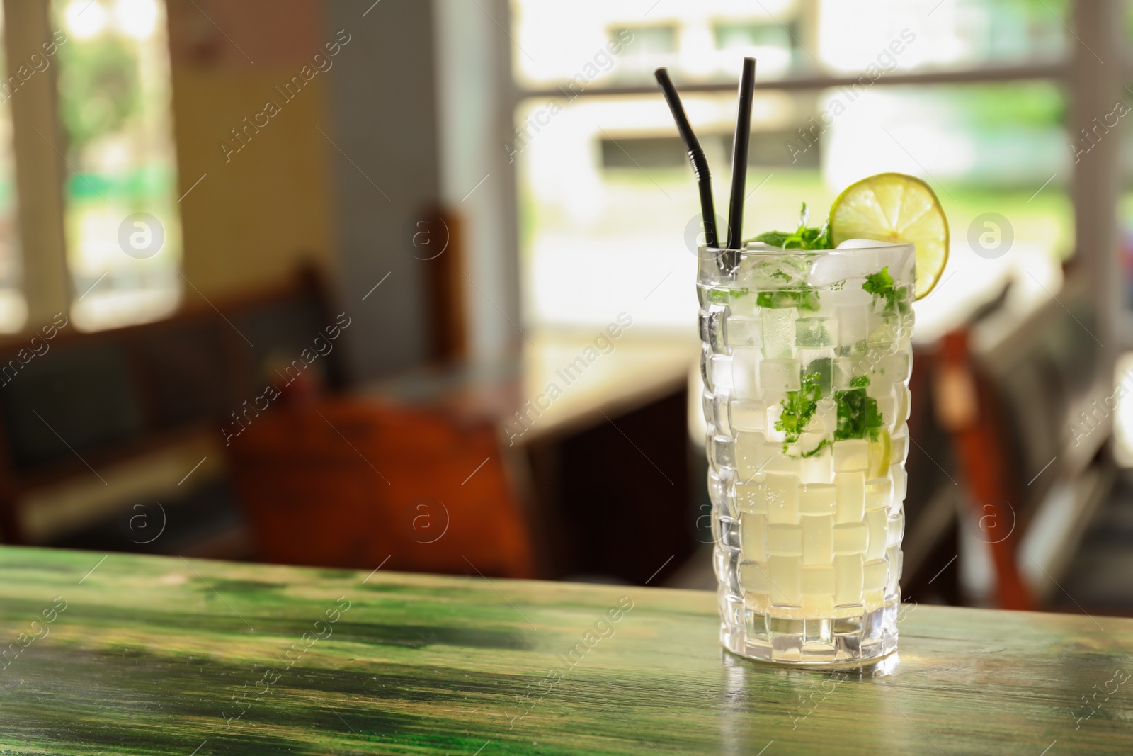 Photo of Glass of delicious cocktail with ice on table in bar